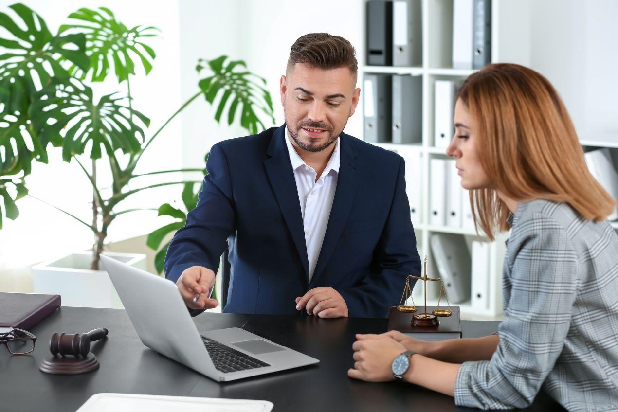 Ein Anwalt in einem formellen Anzug erklärt einer Mandantin am Laptop juristische Details. Symbolisiert die professionelle Mandantenorientierung der Kanzlei Ra-Hartung.