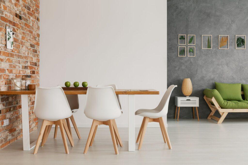 Modernes Esszimmer mit Esstisch aus Holz, weißen Stühlen, grünen Akzenten und einer grauen Wand mit stilvollen Pflanzenbildern.